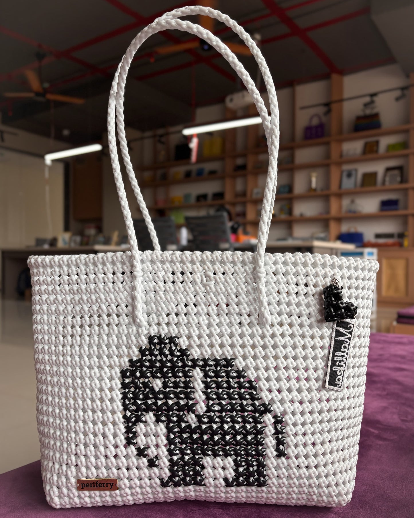 White knitted handbag with an elephant knitted design in the middle, placed on a table in a store.