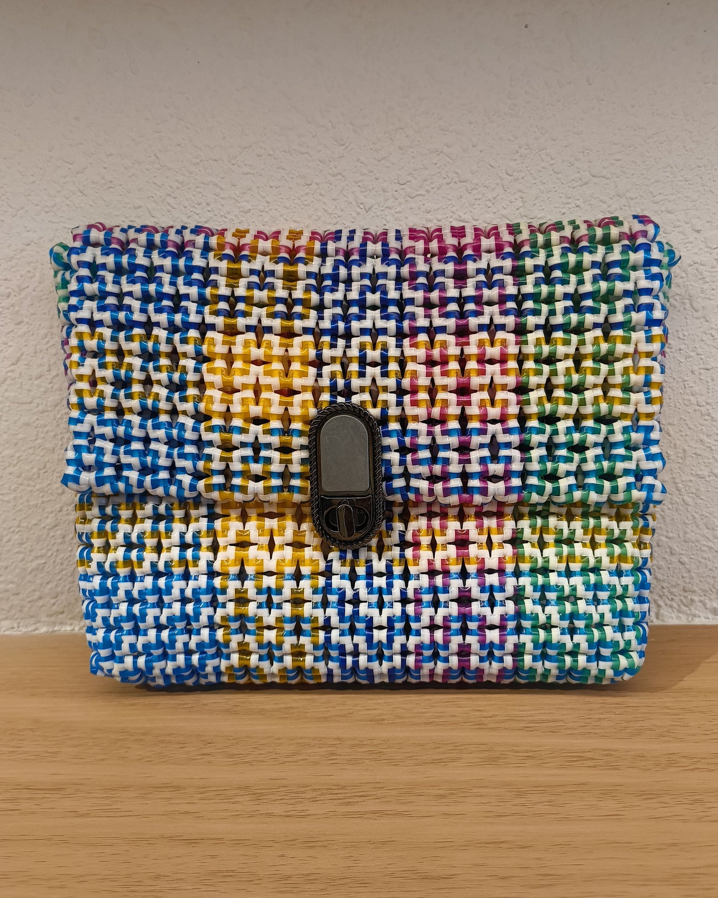 Rainbow colored knitted pouch with a metallic buckle on a wooden surface.