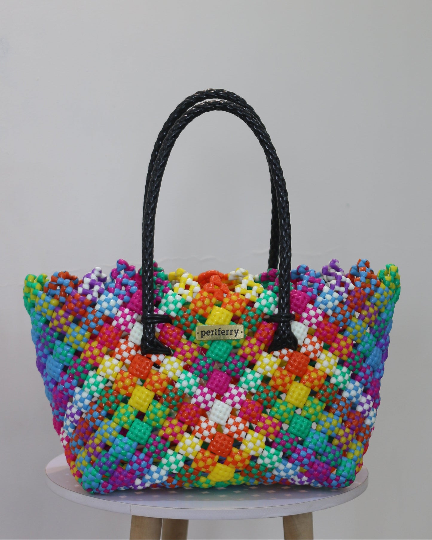 Colorful knitted handbag on a white stool against a gray background