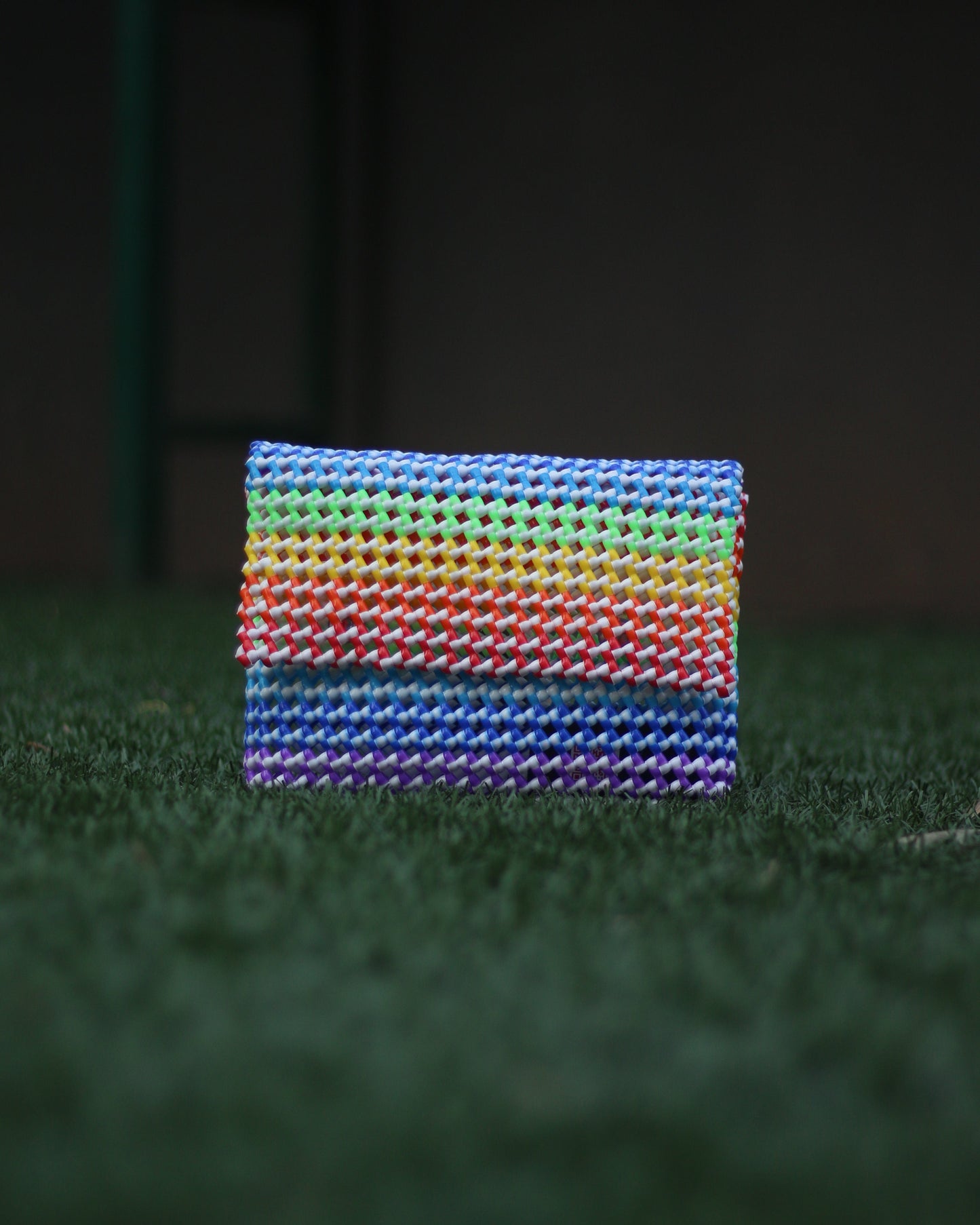 Rainbow colored knitted clutch placed on a grass floor
