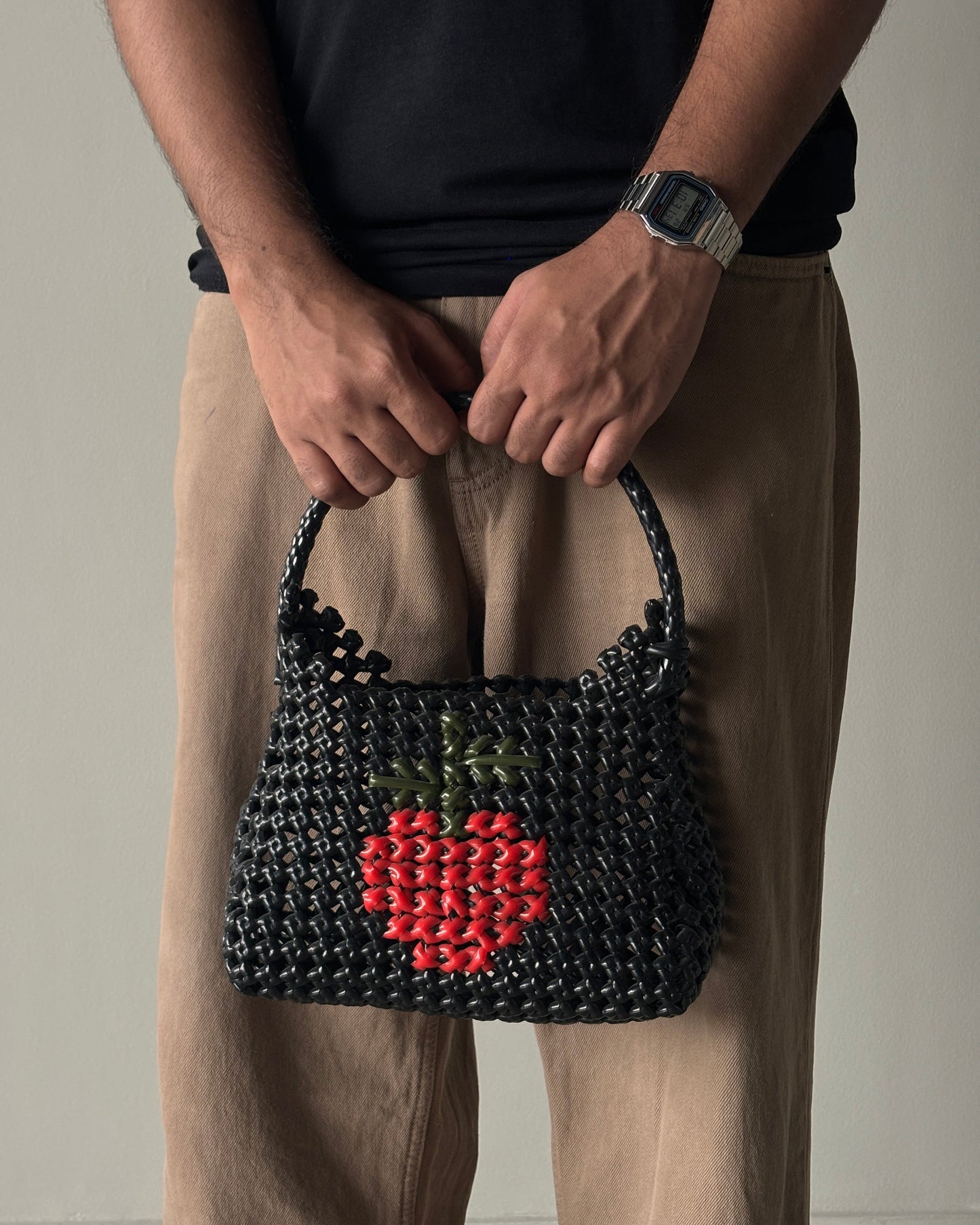Person holding a black knitted handbag with a red apple design in the middle, on a neutral background