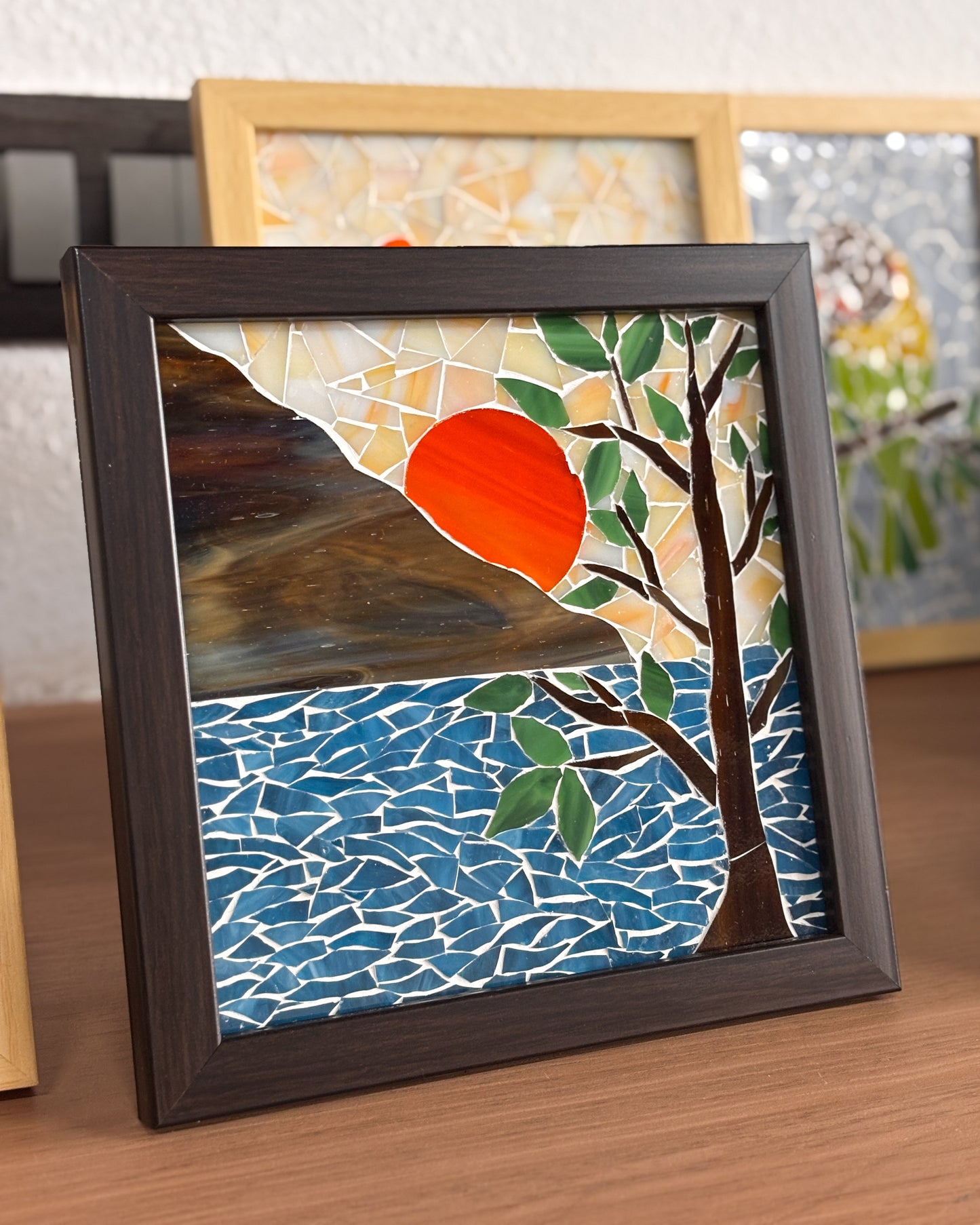 Framed mosaic artwork with a sunset over water and tree design.