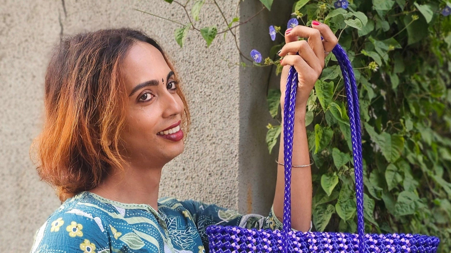 Woman holding a blue beaded bag against a green leafy background