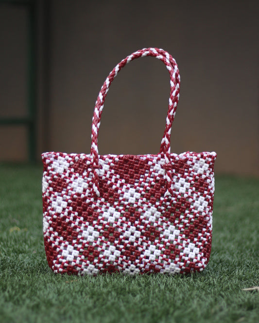 Red and White knitted handbag with a braided handle, placed on a grass surface with blurred background.