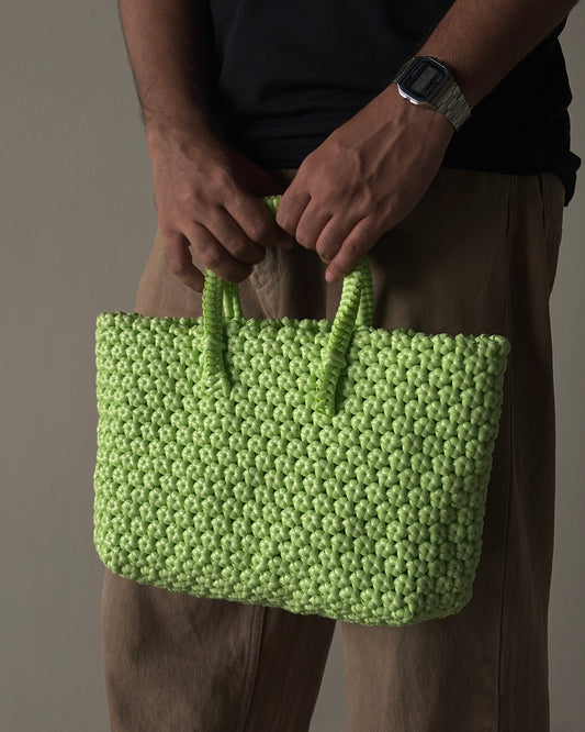Green knitted handbag held by a person with a neutral background