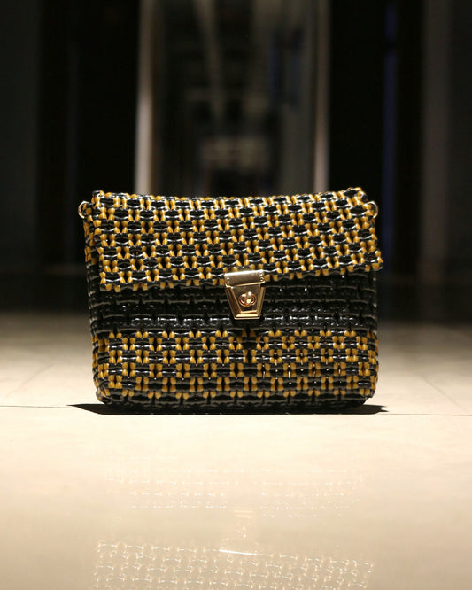 Golden and Black knitted clutch with a metallic clutch placed on a floor with dark background.