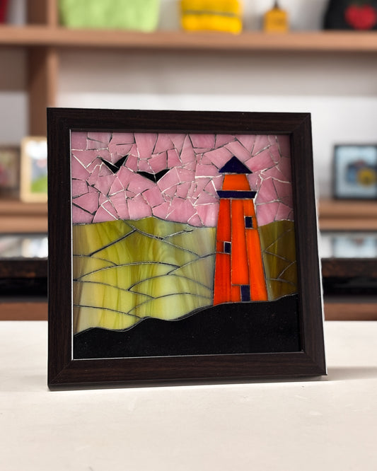 Framed mosaic artwork of a lighthouse on a table with a blurred background