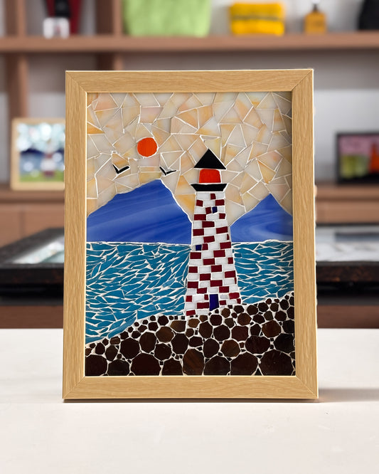 Mosaic artwork of a lighthouse and sun in a wooden frame.