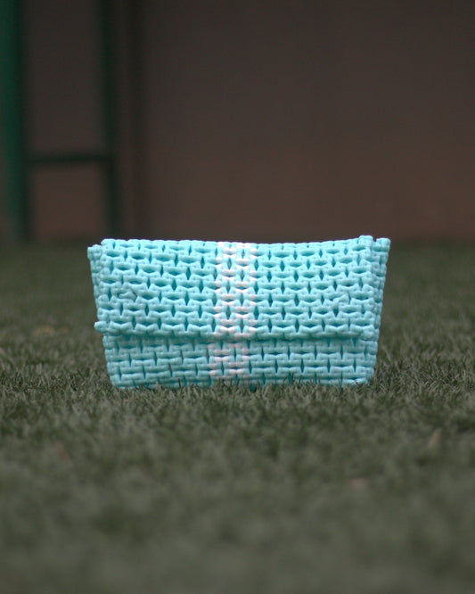 Turquoise knitted pouch on a grassy surface with blurred background.