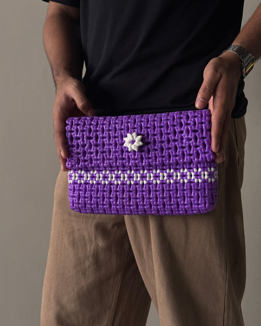 Purple knitted clutch with a white knitted flower detail in the middle, held by a person against a neutral background