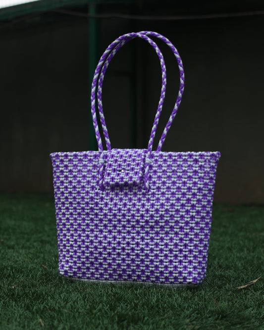 Purple knitted handbag with a textured pattern and a braided handle on a grass