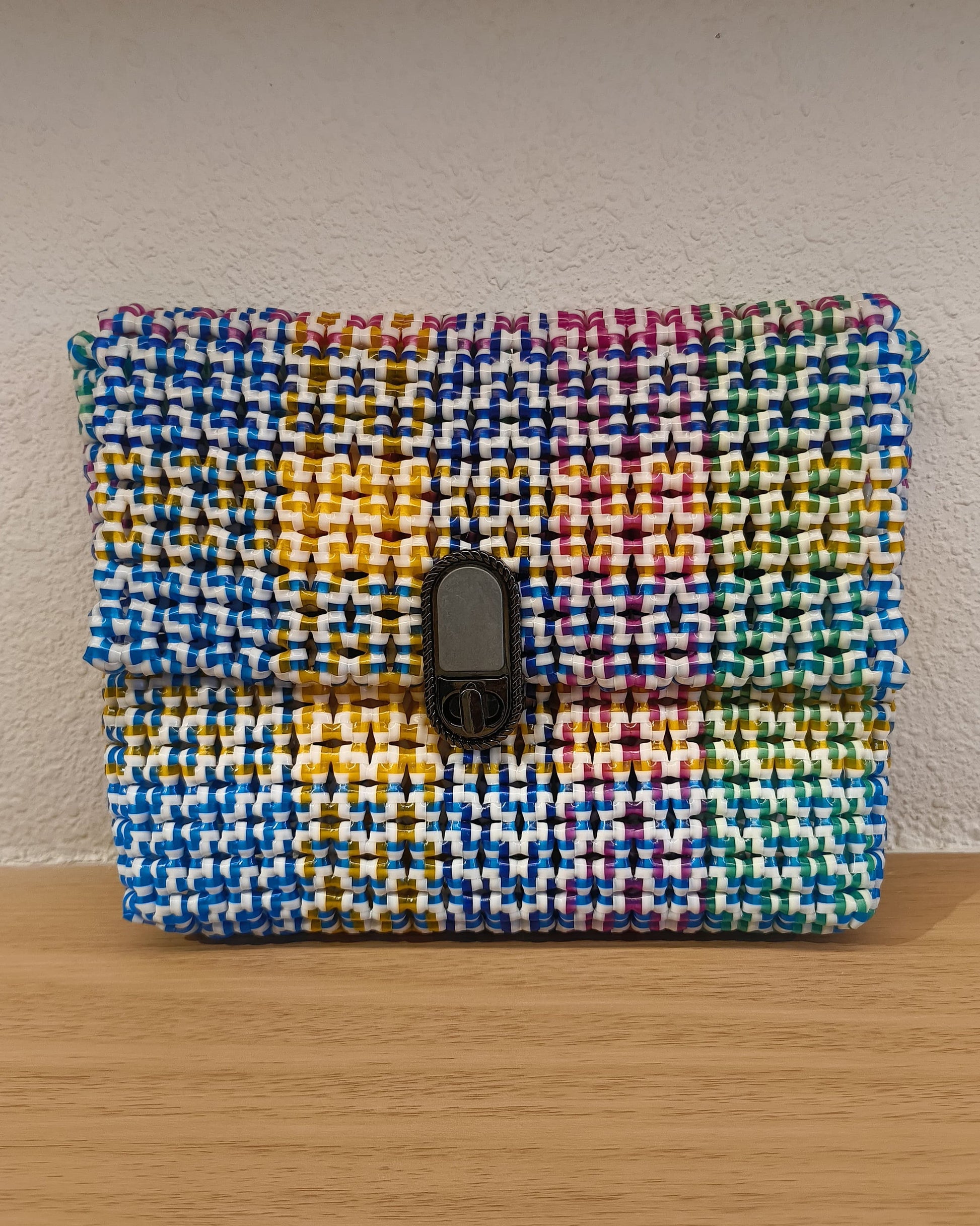 Rainbow colored knitted pouch with a metallic buckle on a wooden surface.