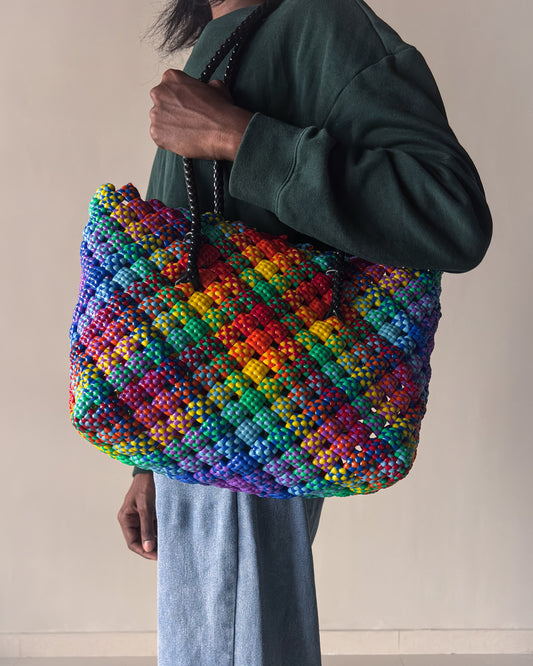 Person holding a rainbow colored knitted handbag against a neutral background