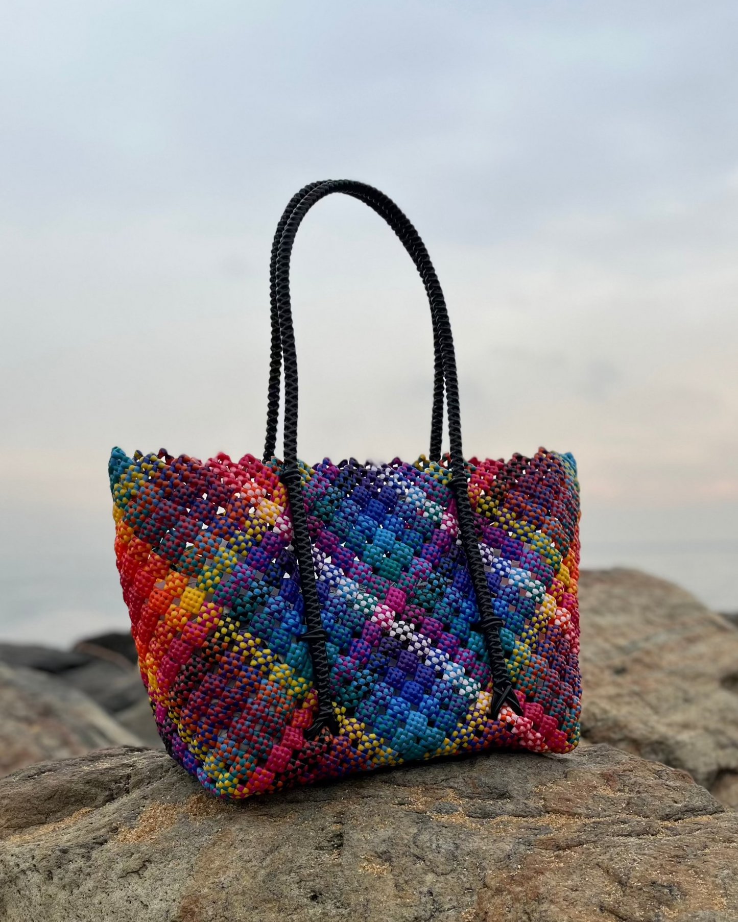 Rainbow colored knitted bag on a rock with a cloudy sky background