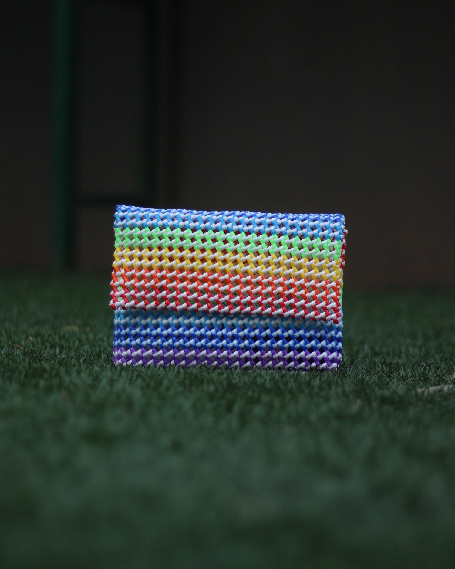 Rainbow colored knitted clutch placed on a grass floor
