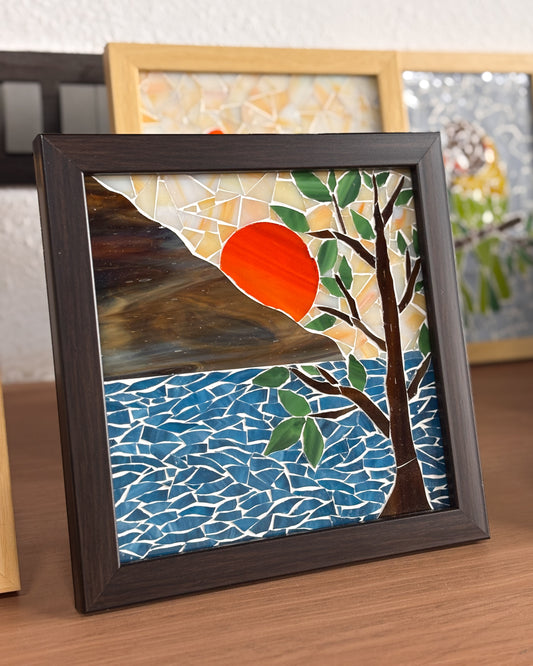 Framed mosaic artwork with a sunset over water and tree design.